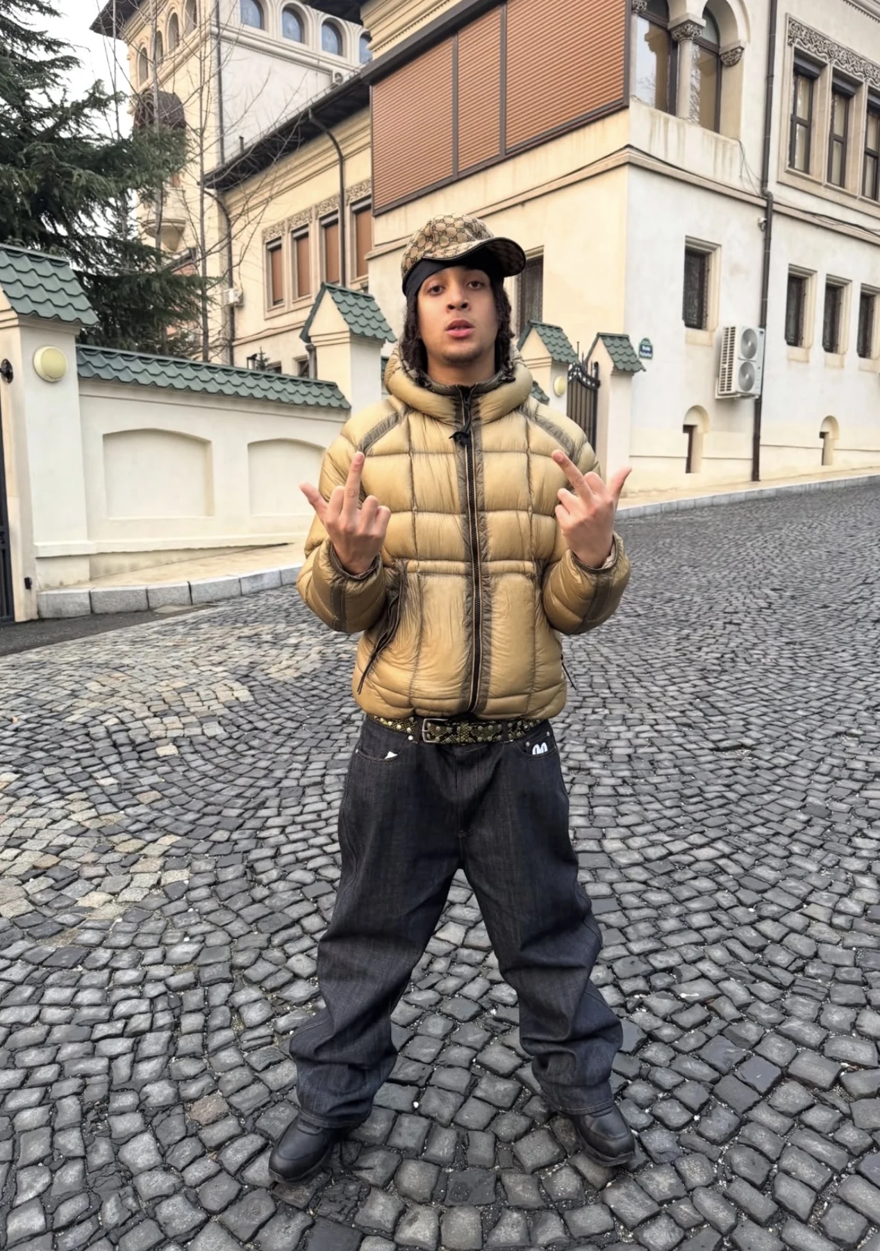 FIN wearing a gold puffer jacket on a cobbled street