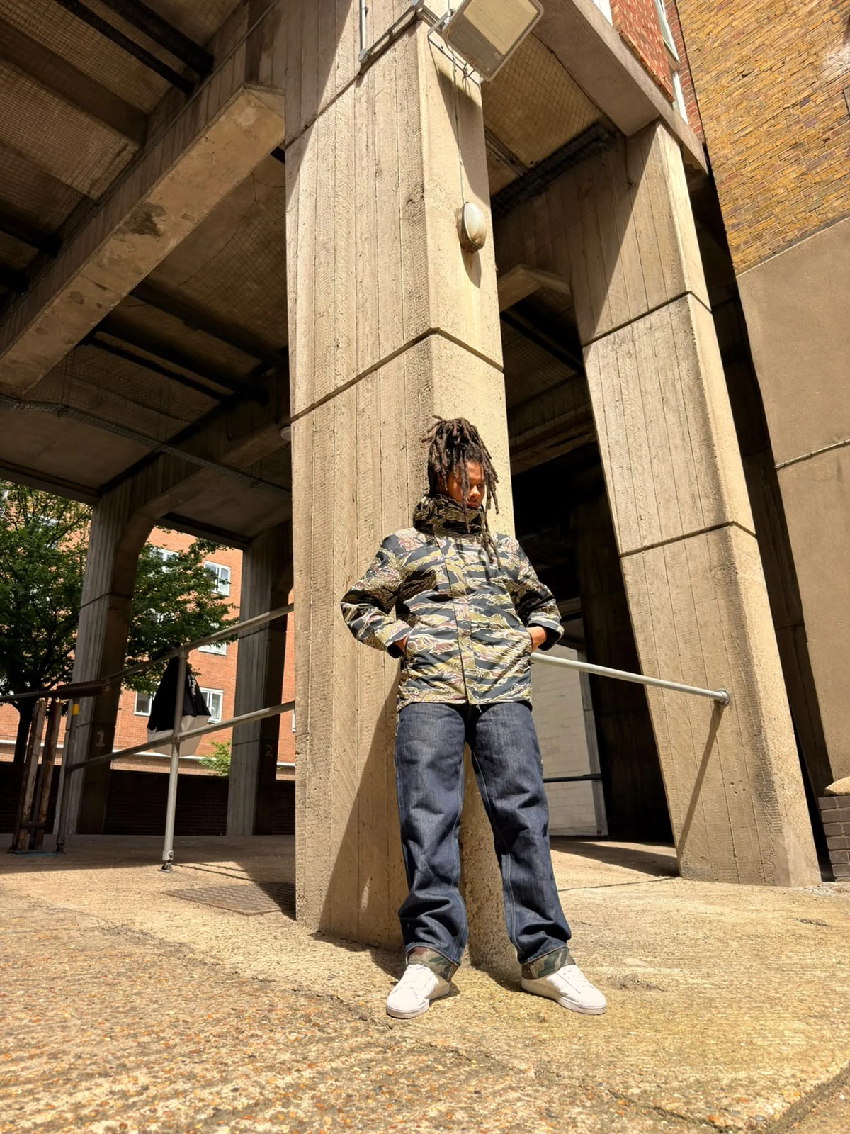 LZEE wearing a camouflage jacket and jeans beside concrete columns