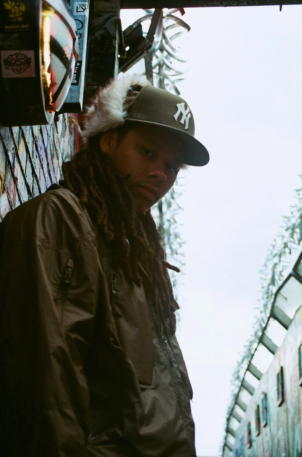 LZEE wearing a dark jacket and cap beside a brick wall
