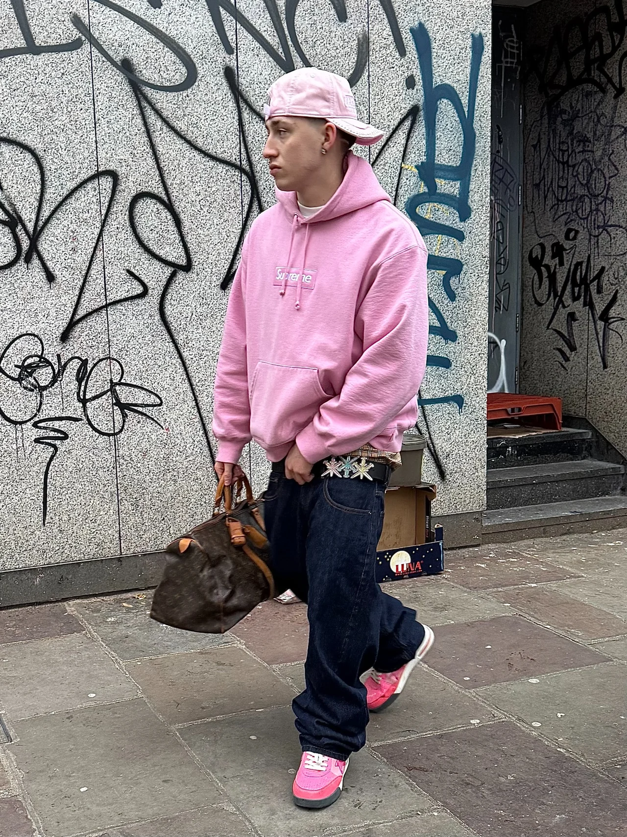 TED wearing a pink Supreme hoodie on a graffiti-lined street